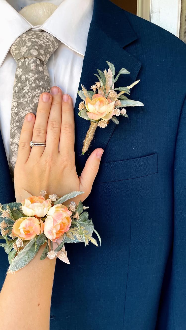 Peach floral boutonniere pinned to a navy blue suit lapel next to a matching wrist corsage.