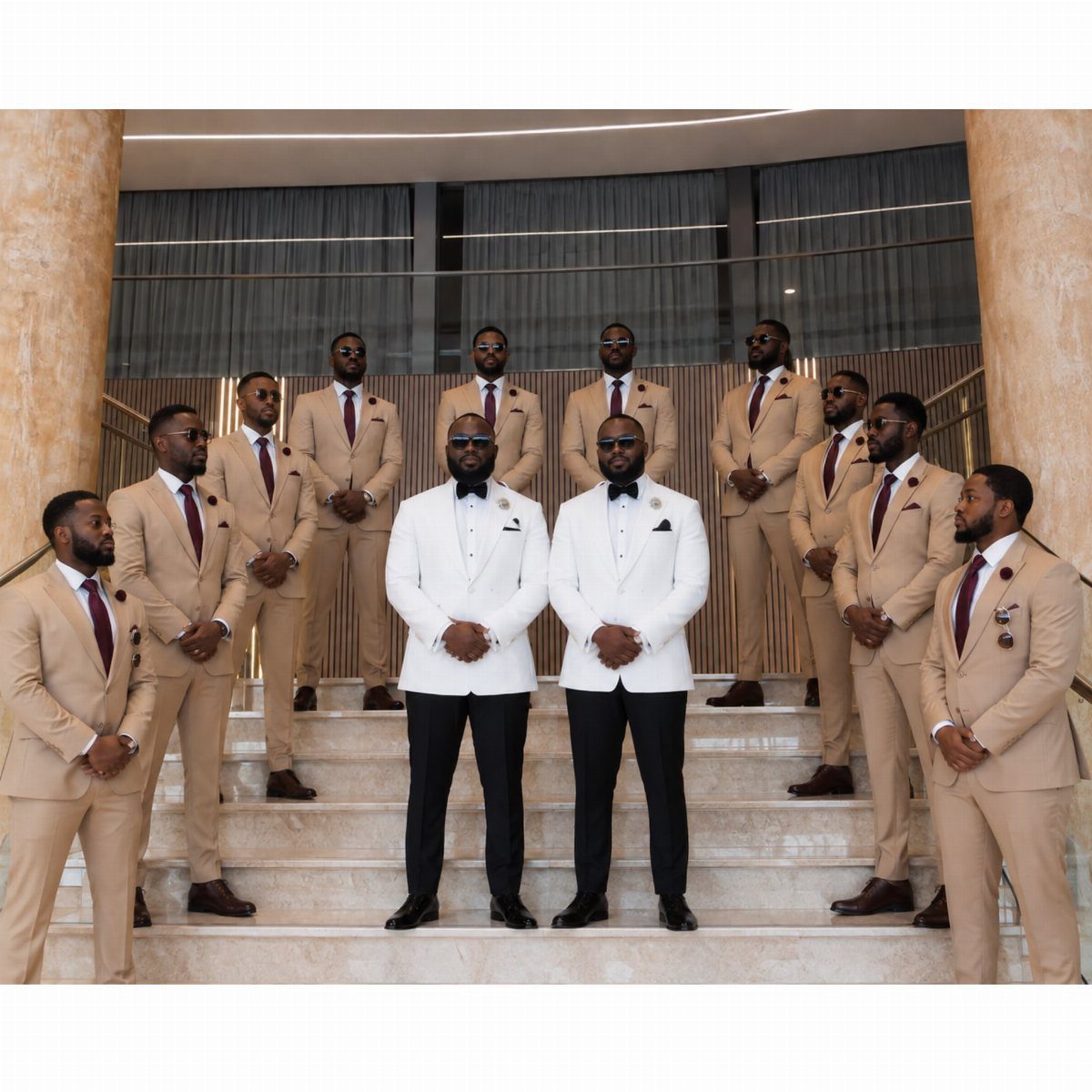 Men in tan suits and white blazers posing together on a wide staircase.