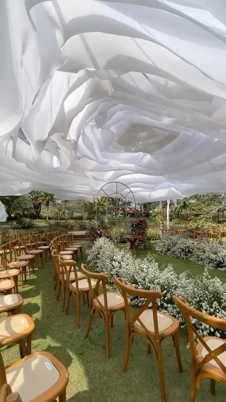 Wooden chairs arranged on a green lawn under a white fabric canopy for an outdoor wedding.