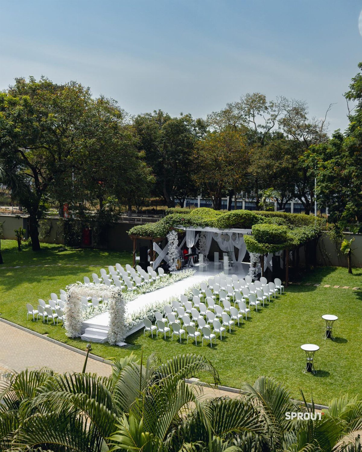 White wedding chairs and an altar arranged on a green lawn in a garden setting.