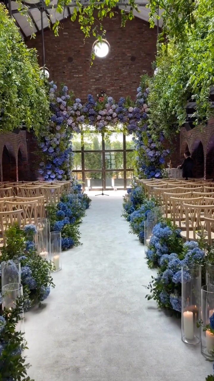 A wedding ceremony aisle lined with blue hydrangeas and candles under a brick ceiling.
