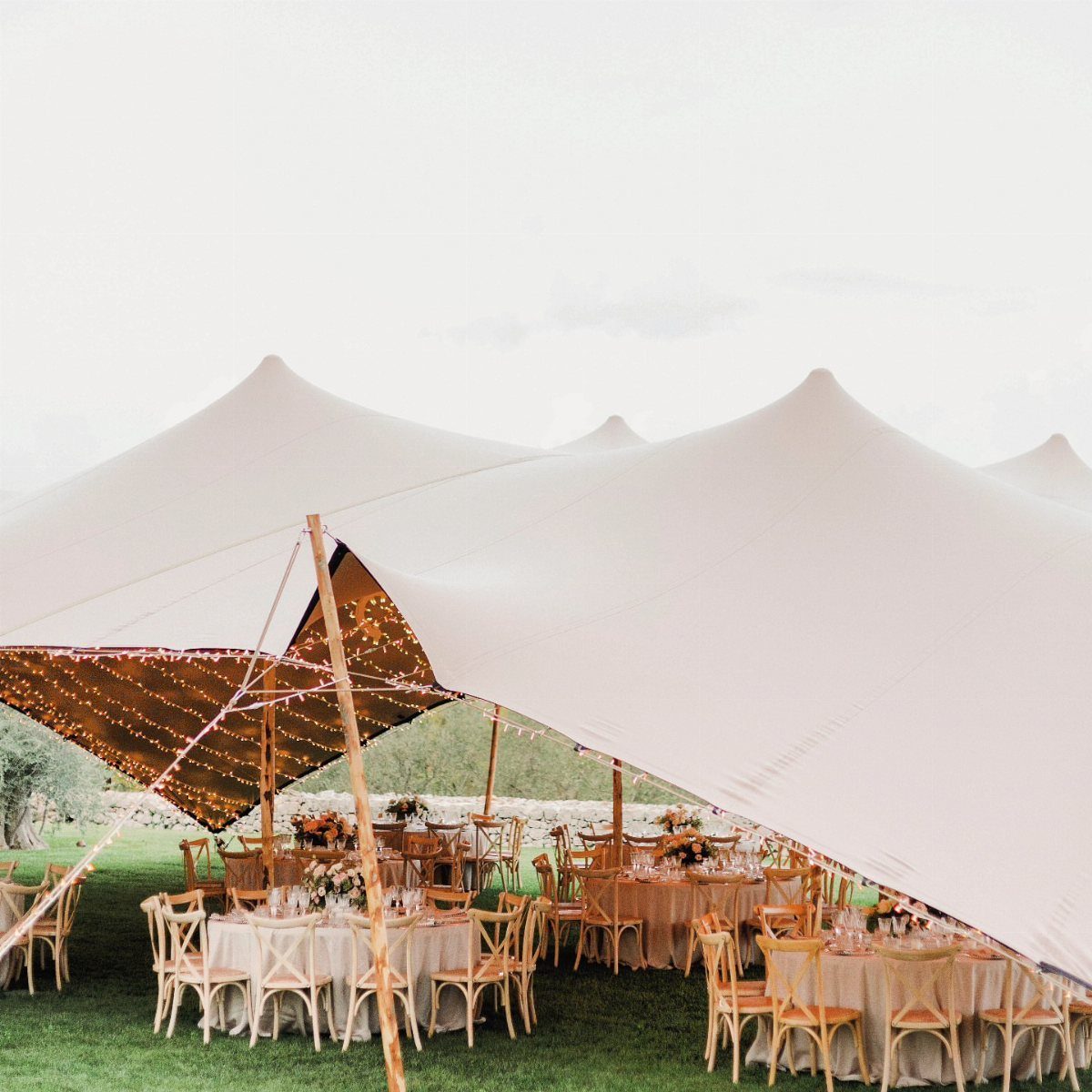Large white peaked event tent set up on a lawn with decorated dining tables underneath.