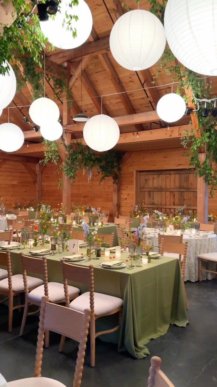 Wedding reception tables set with green linens and flowers inside a rustic wooden barn.