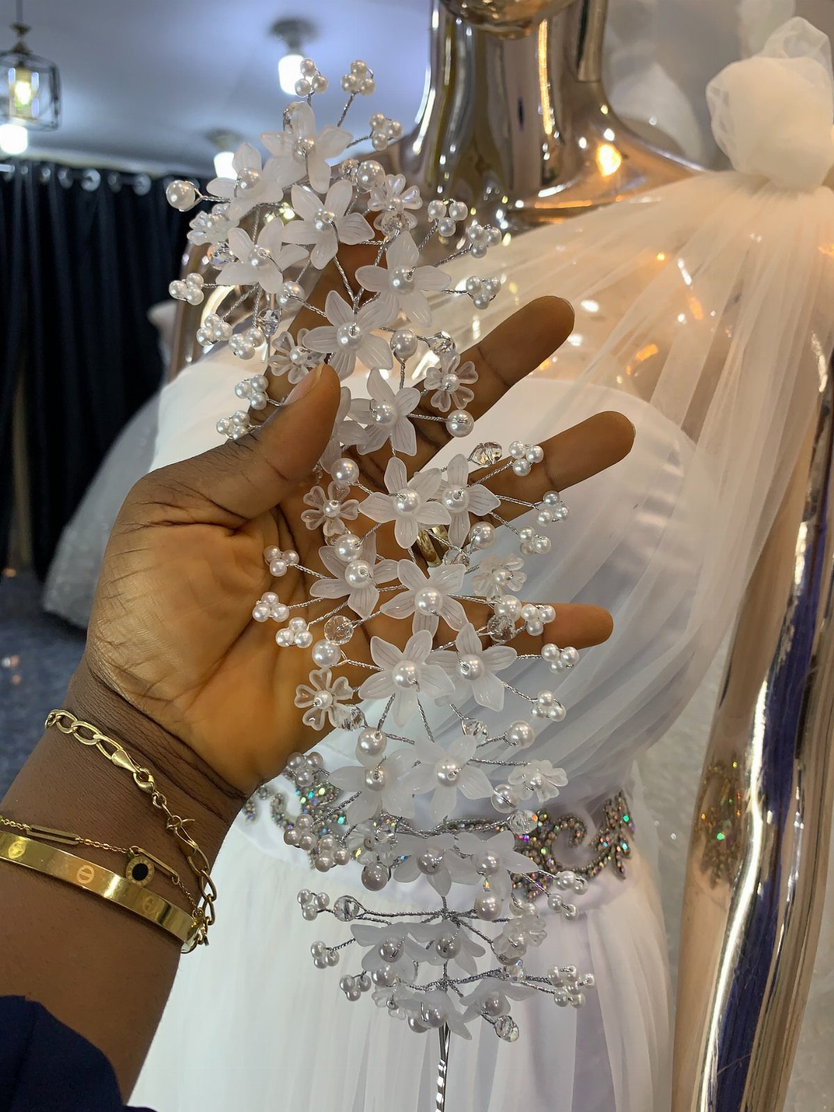 A hand holding a silver floral hairpiece decorated with white flowers and pearls.
