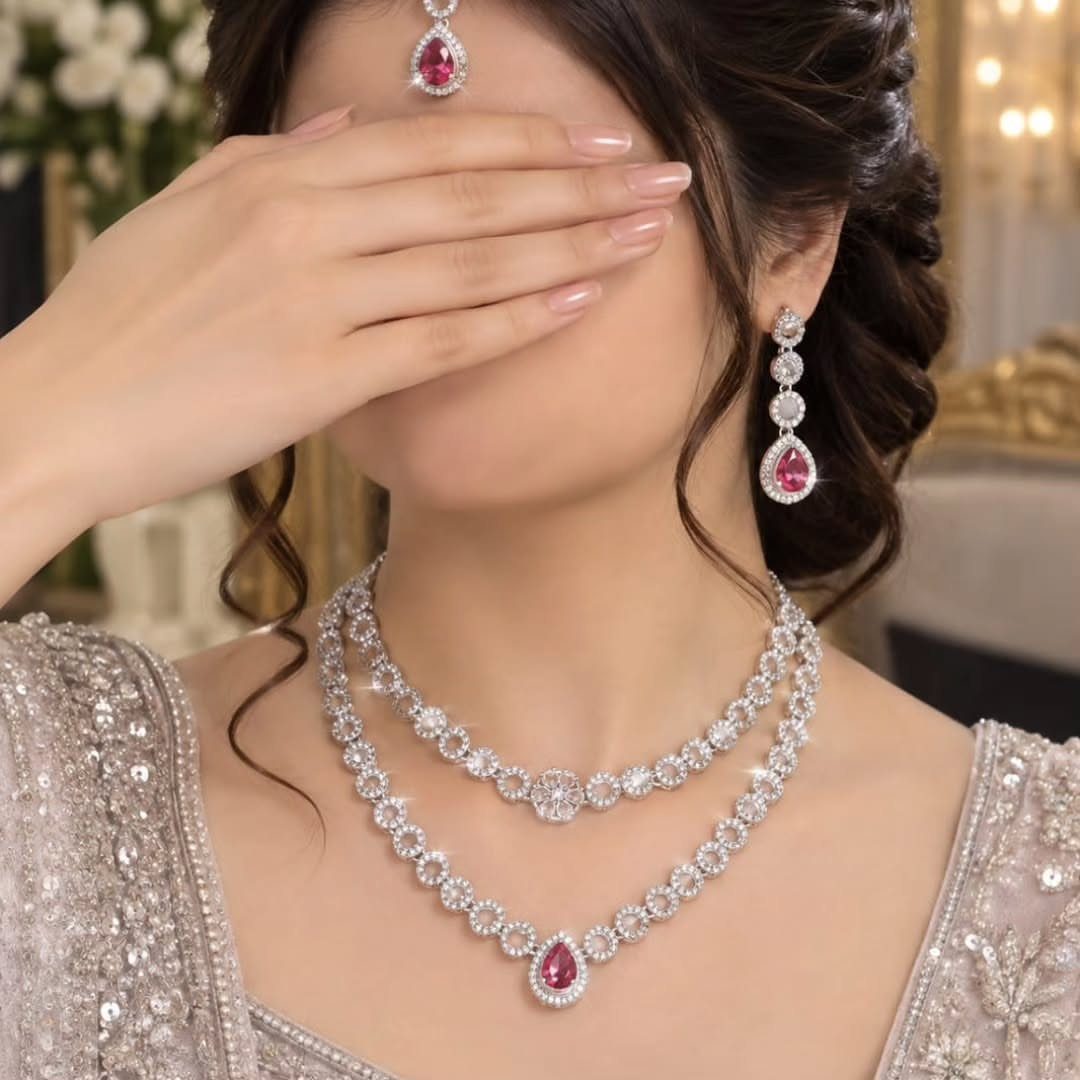 Woman wearing layered silver necklaces with pink gemstones and matching earrings.