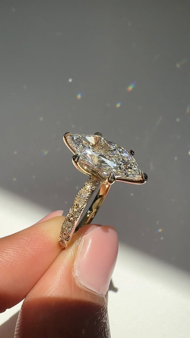 A large marquise-cut diamond ring with a pavé gold band held by a hand.
