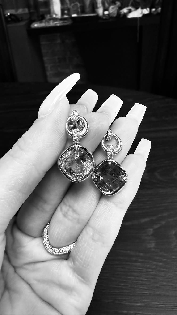 A hand holding large, faceted gemstone statement earrings and wearing a sparkling ring.