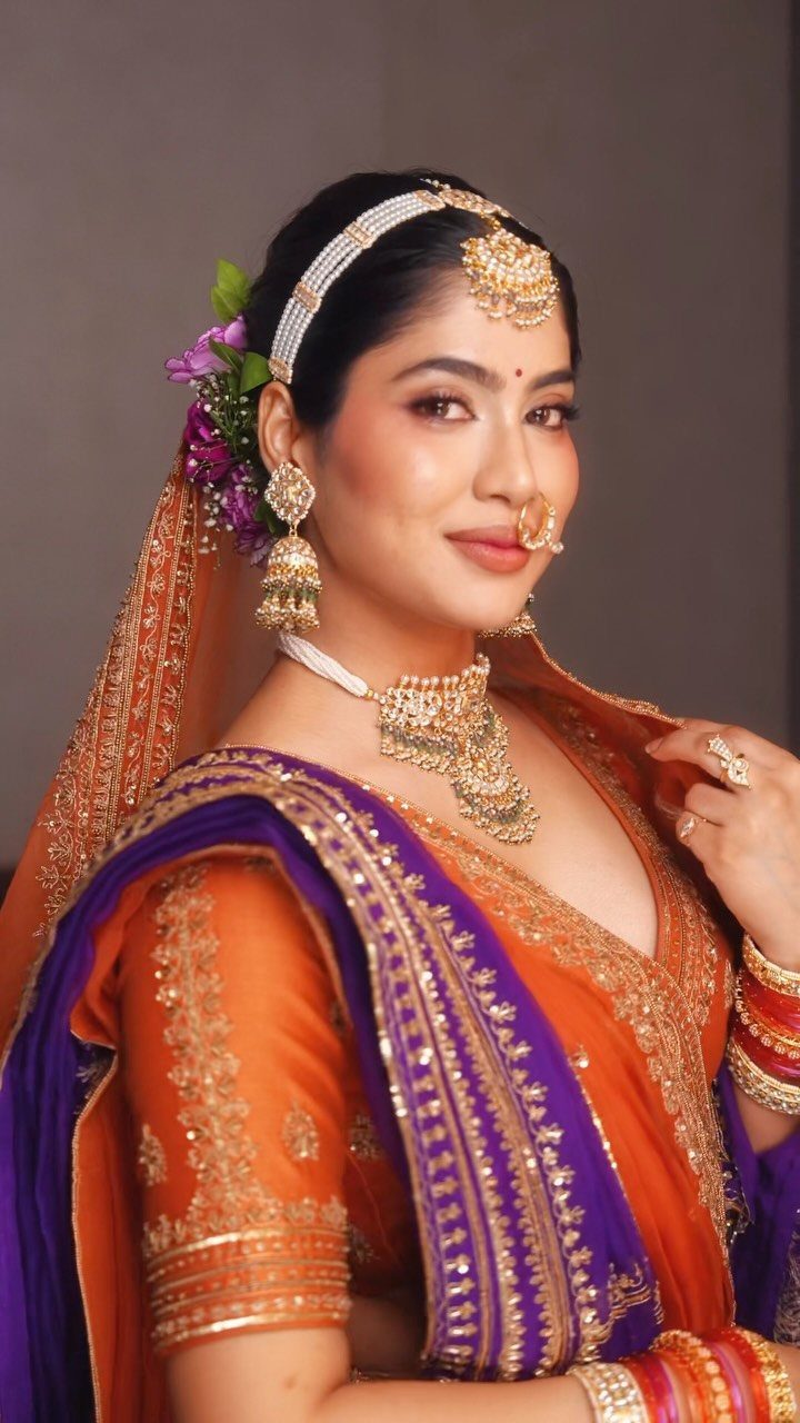 A woman in traditional Indian bridal clothing wearing gold jewelry and colorful clothing.