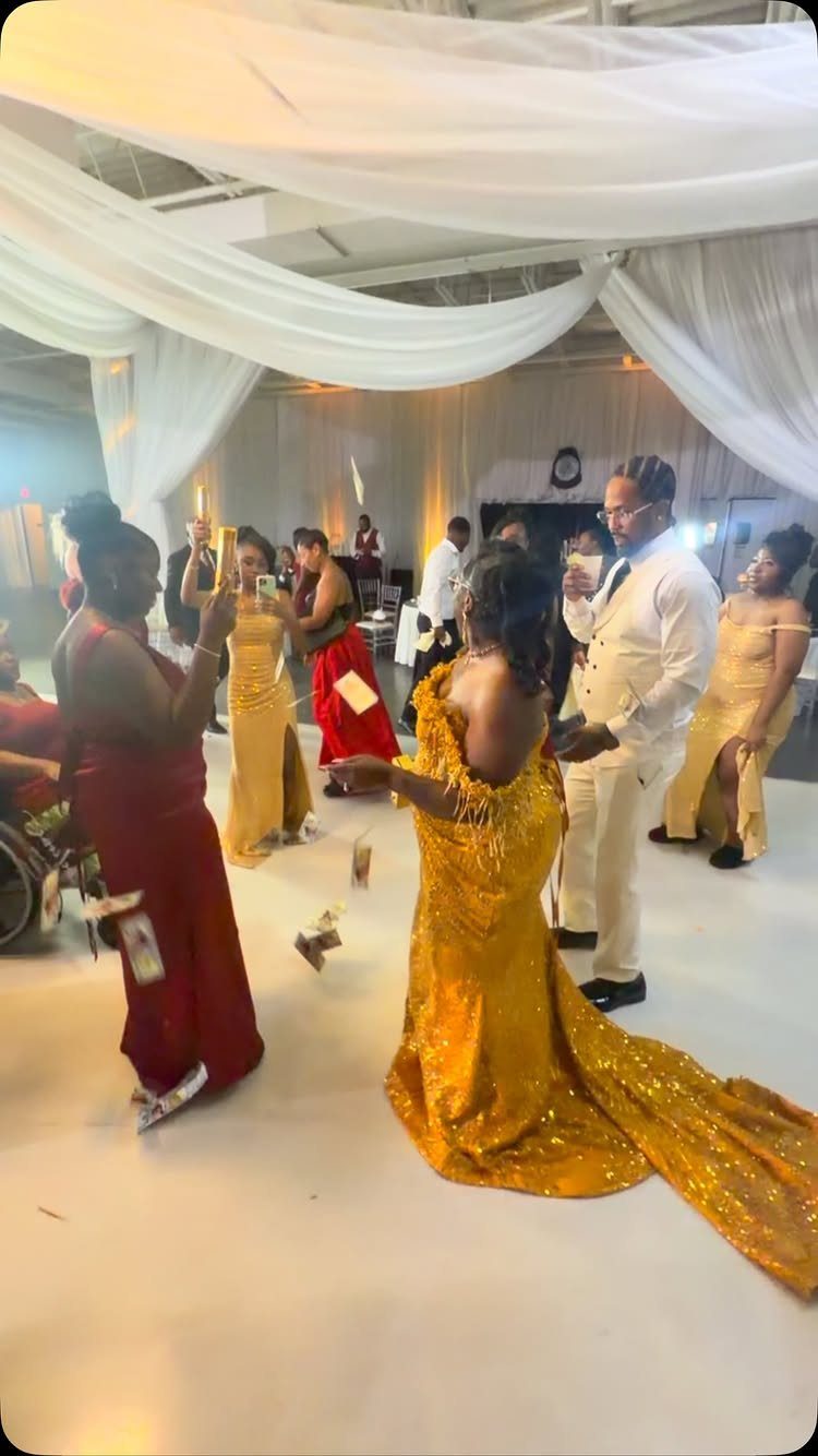 A bride and groom dance while guests throw money around them during a wedding reception.