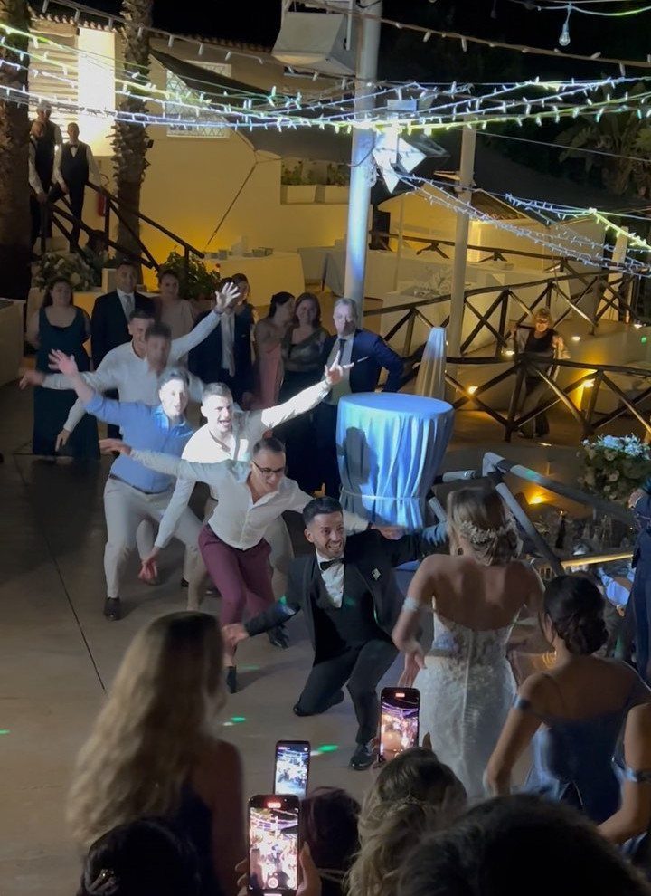 People in formal wear performing a choreographed dance outdoors under string lights at night.