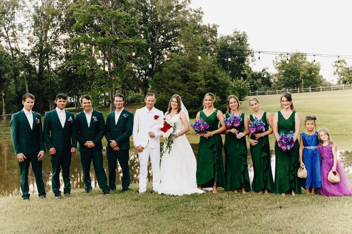 Wedding party in forest green suits and dresses posing on a grassy field.