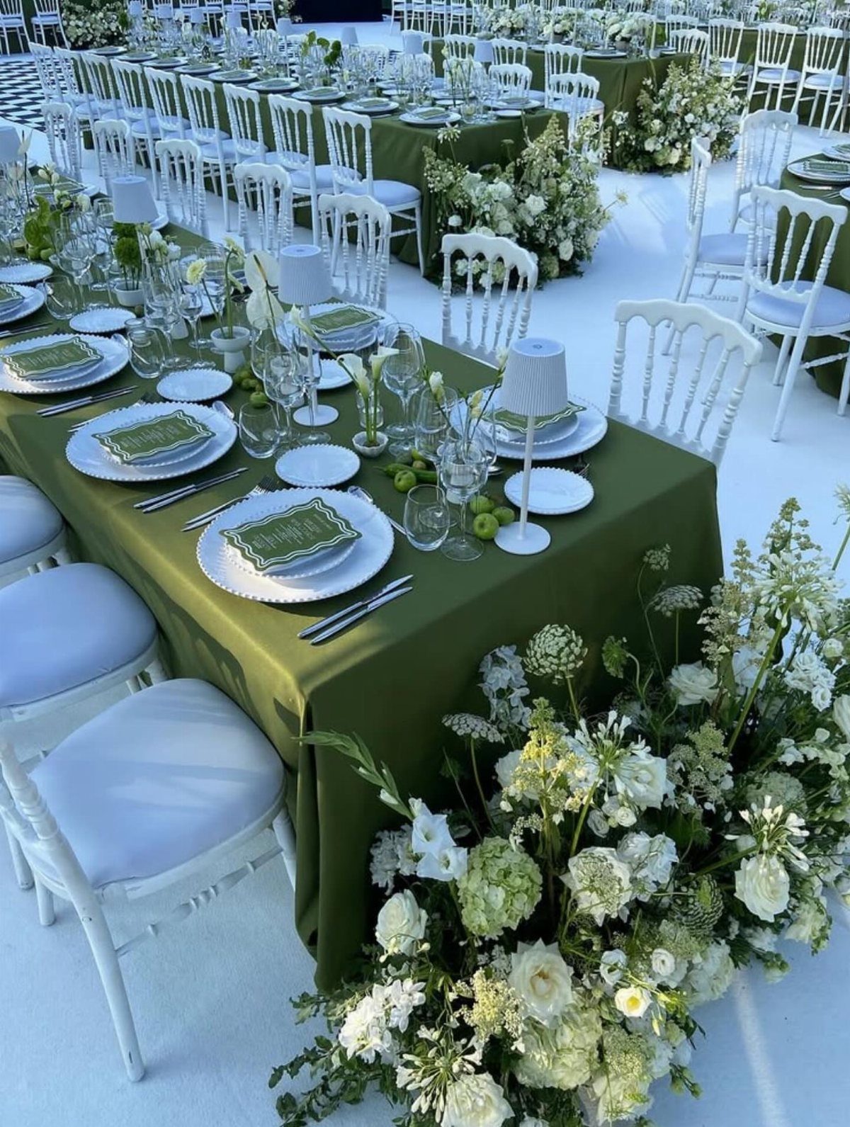 Long banquet tables with olive green tablecloths, white plates, and lush white floral arrangements.
