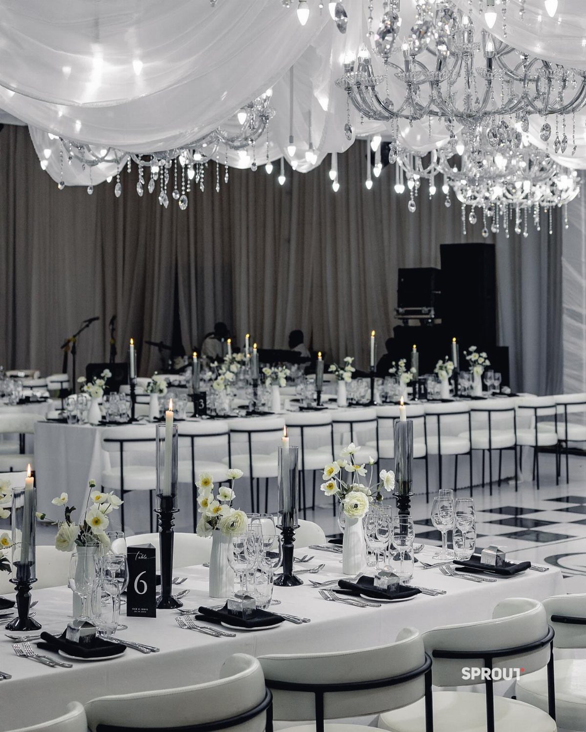 Formal wedding reception tables with black accents, white flowers, and crystal chandeliers in a ballroom.