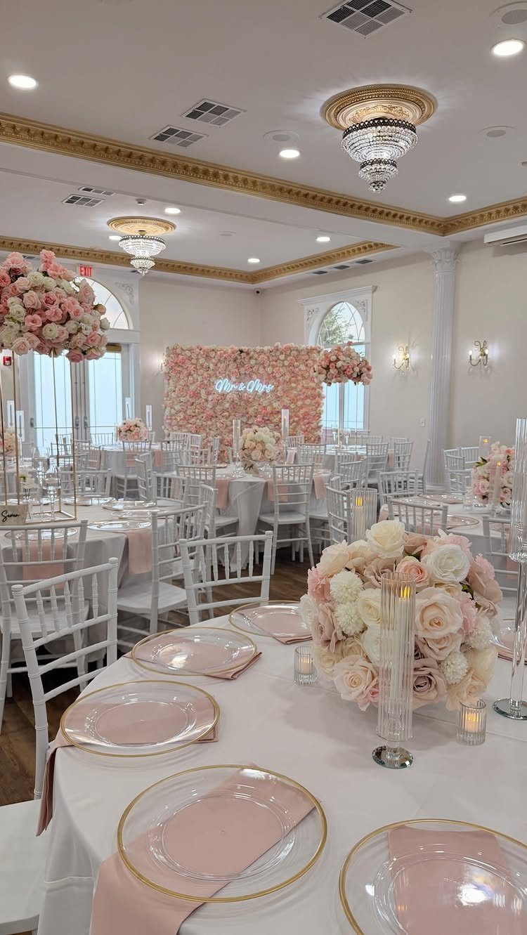 Wedding reception tables decorated with blush pink napkins, cream roses, and gold-rimmed plates.
