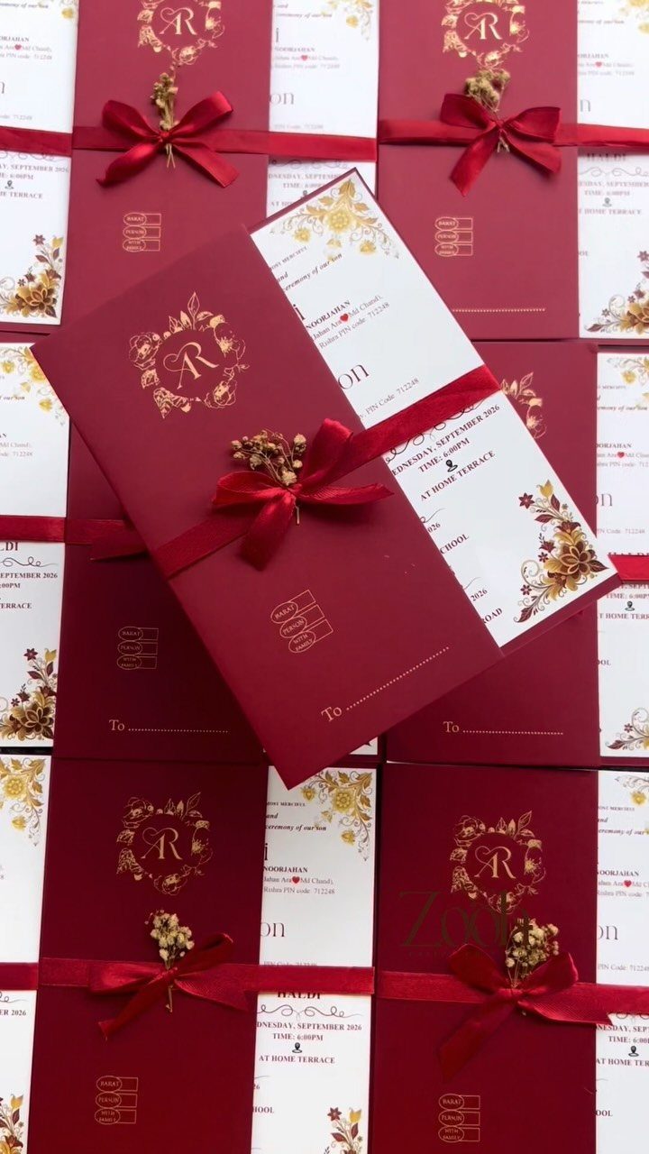 Burgundy wedding invitations with gold floral patterns and red ribbon accents arranged in a group.