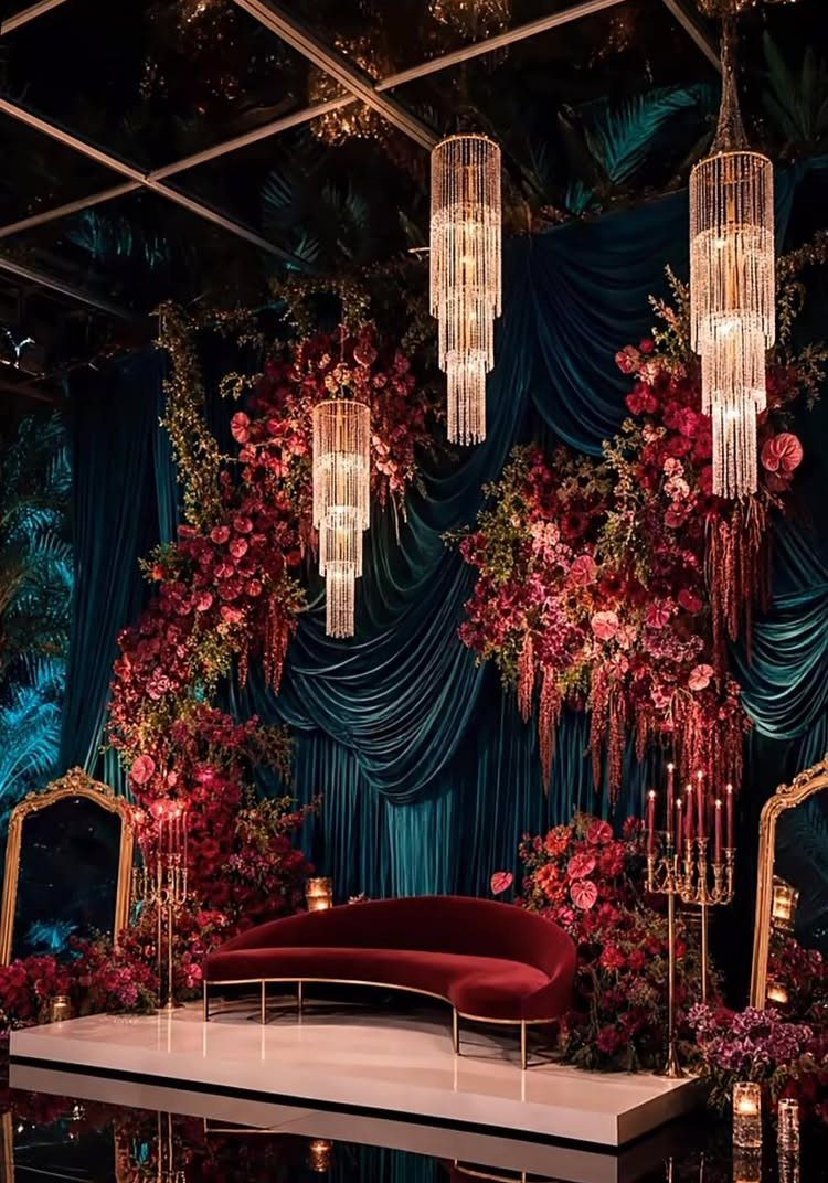 A luxurious wedding stage with teal drapes, pink floral arrangements, and a red velvet sofa.