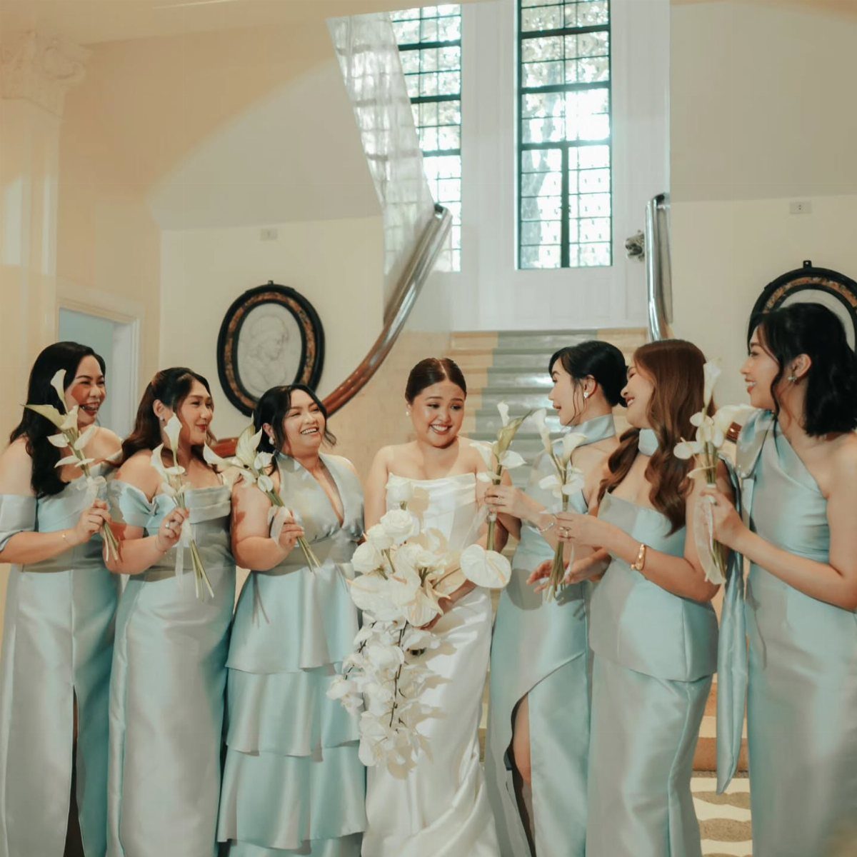 Bridesmaids in light blue satin dresses and a bride in white holding white flowers.