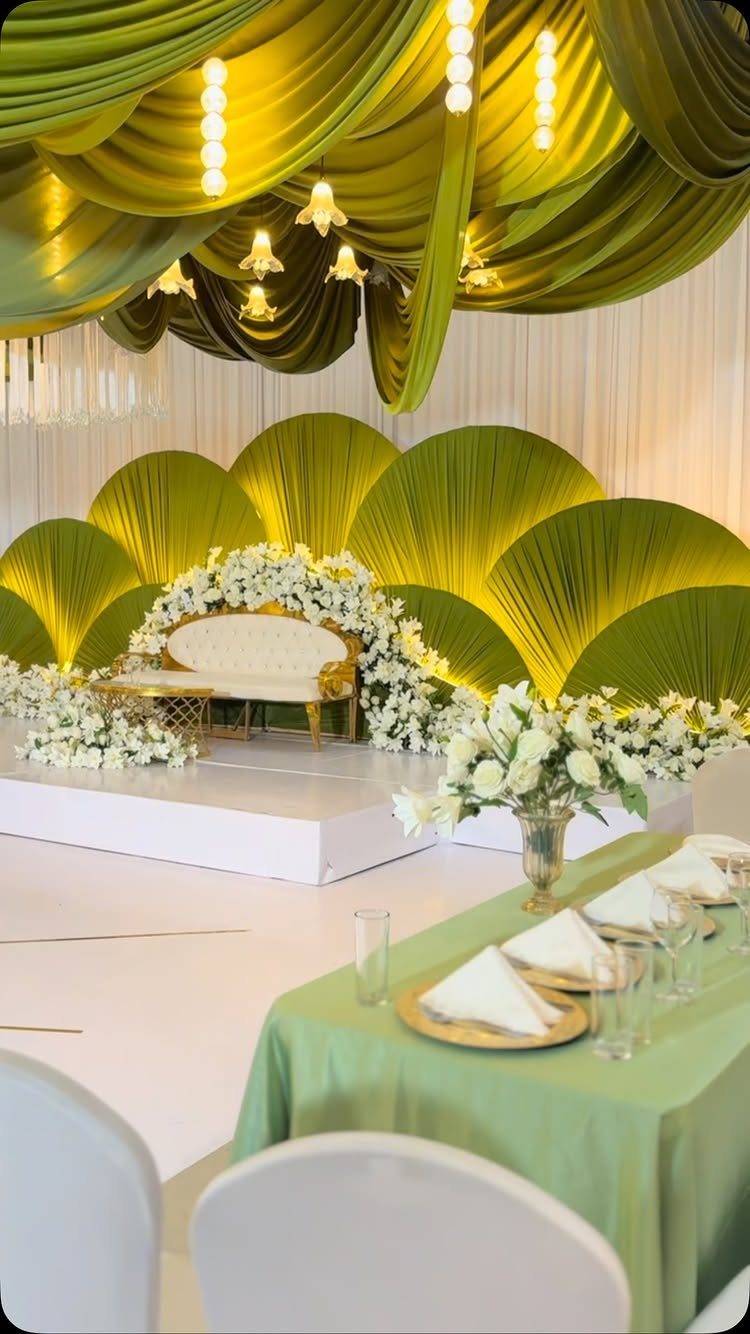 Green draped ceiling and palm leaf decor surrounding a white wedding sofa and floral arrangements.