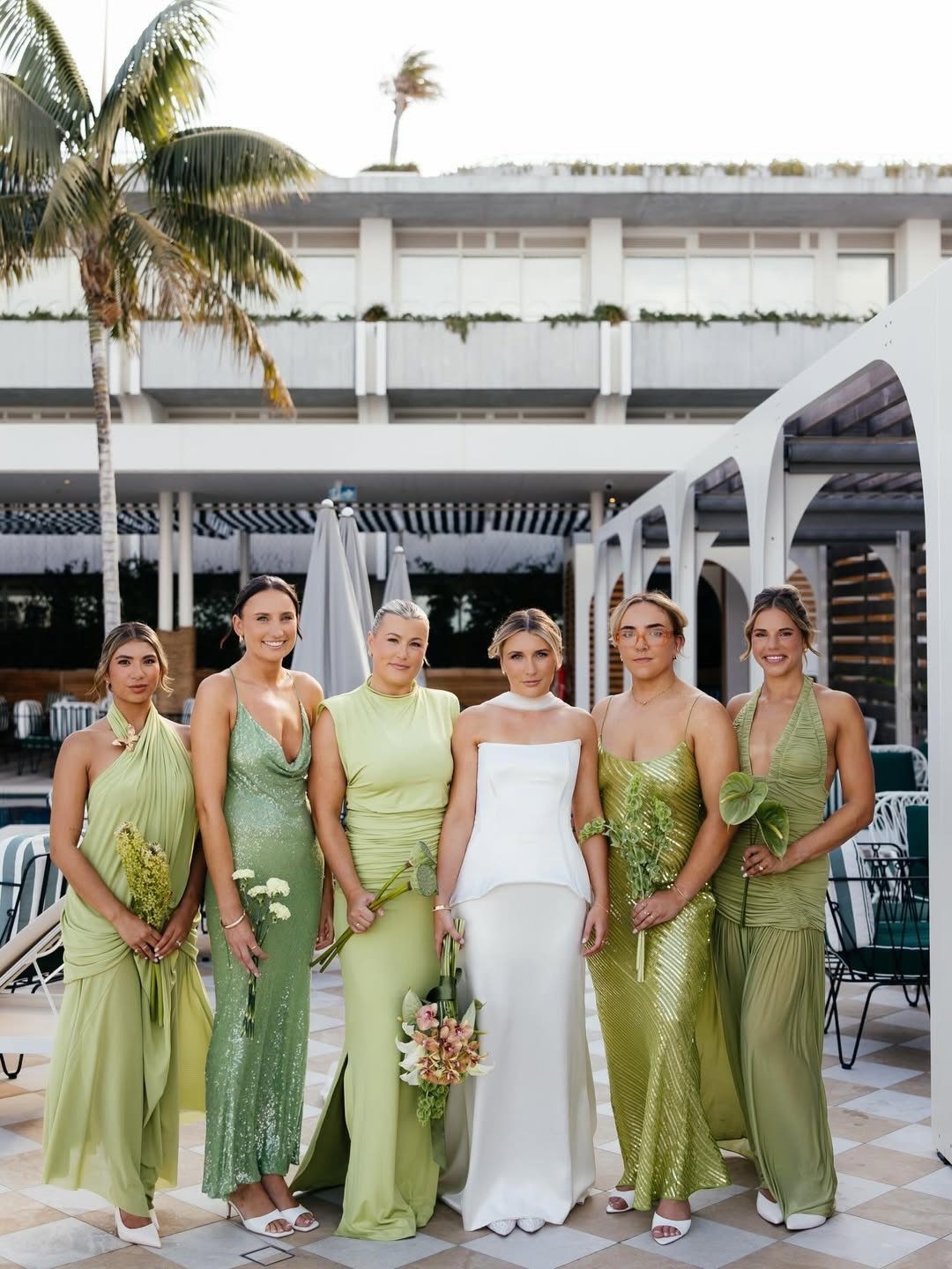Five bridesmaids in various green dresses stand next to a bride in white.
