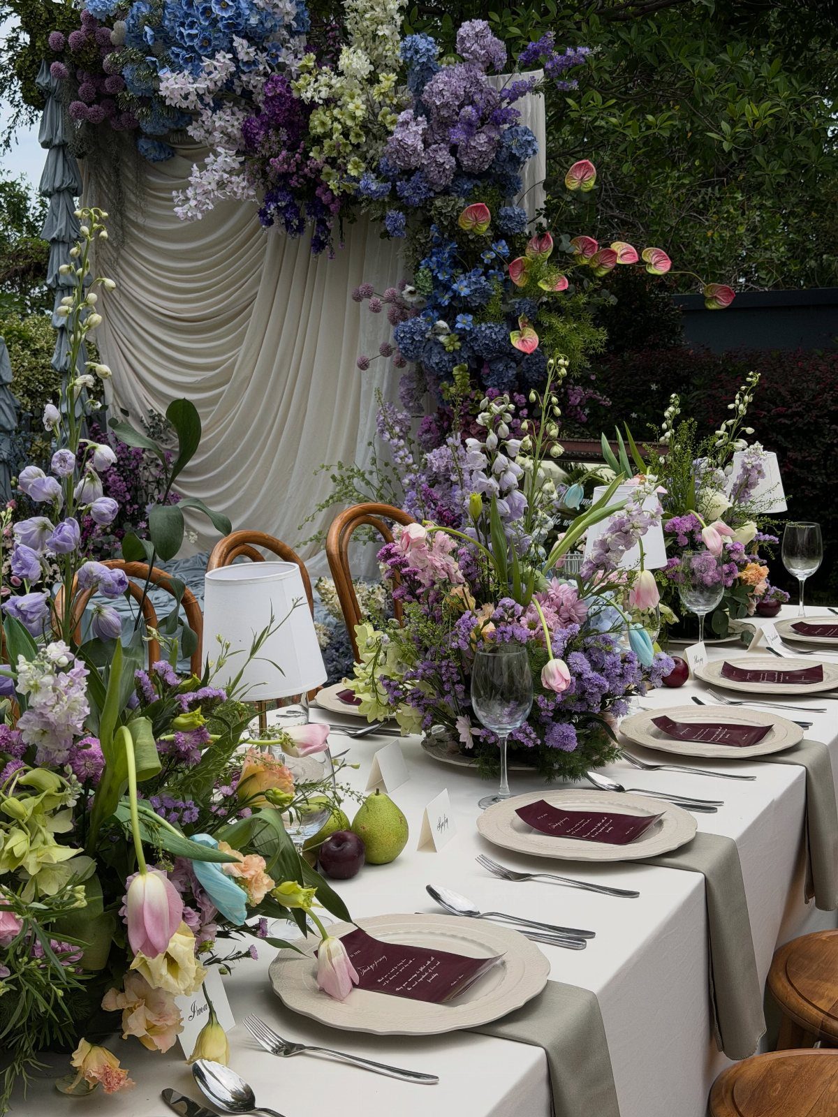 Floral wedding table arrangements featuring purple and blue flowers with white linens and elegant glassware.