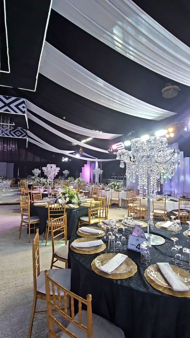Gold Chiavari chairs arranged around banquet tables with black linens and gold chargers in a decorated hall.