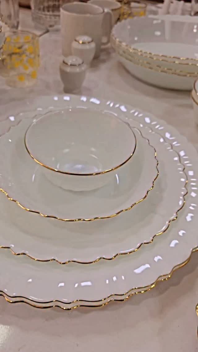 White scalloped ceramic plates with elegant gold rims stacked on a white tablecloth.