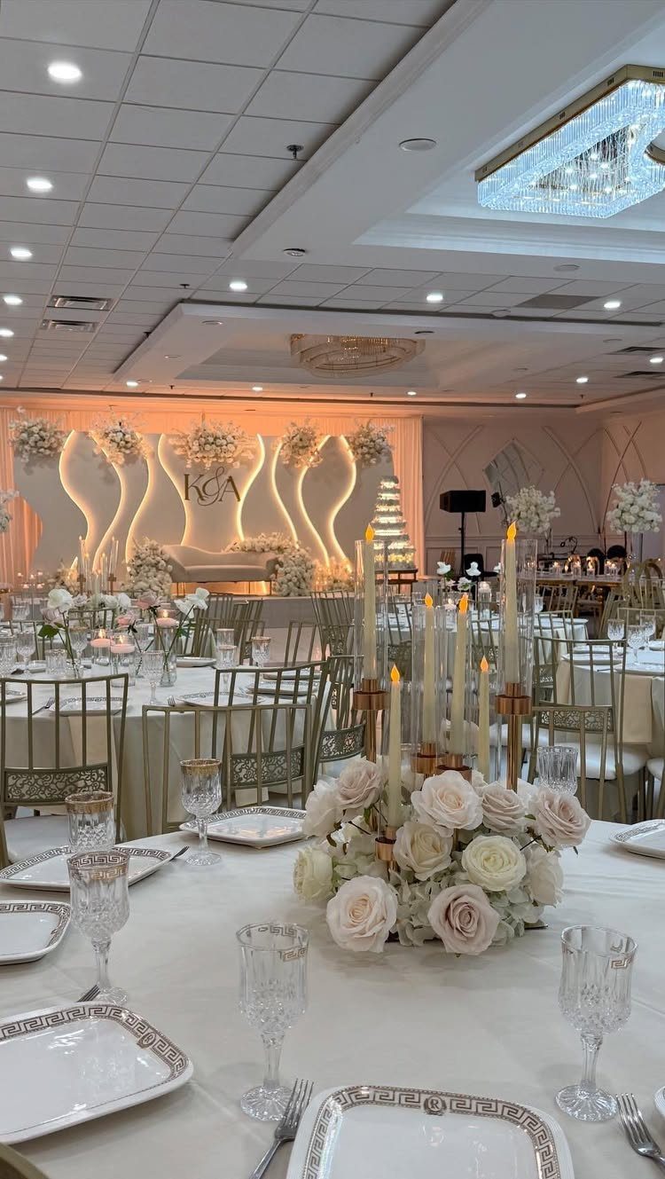 Elegant wedding tables set with white linens, gold-rimmed plates, and white floral centerpieces with candles.